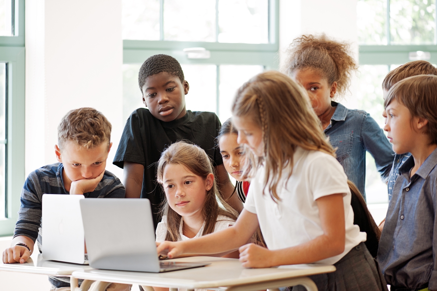 School children using laptop with teacher in the classroom